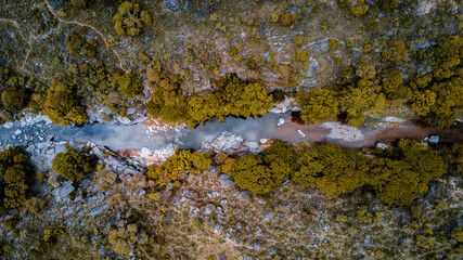 vista área cenital de un arroyo abriéndose camino entre las piedras en una tarde otoñal, con sus aguas cristalinas reflejando las nubes del cielo.