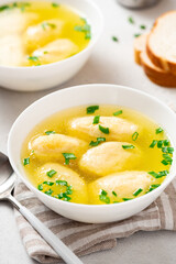 Griessnockerlsuppe. Soup with semolina dumplings in a white bowl on a light concrete background. Bavarian cuisine.