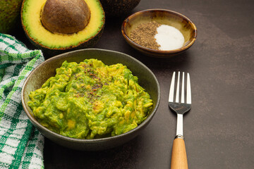 Fresh guacamole on a dish with ingredients for homemade guacamole avocados, lemon, salt, and pepper. Top view. Concept of traditional Mexican preparation