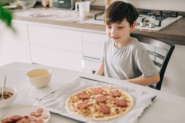 Little kid boy making pizza sitting at the table on the kitchen. Children helping in cooking lifestyle image