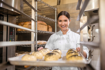 Happy woman putting baking sheet with buns on rack