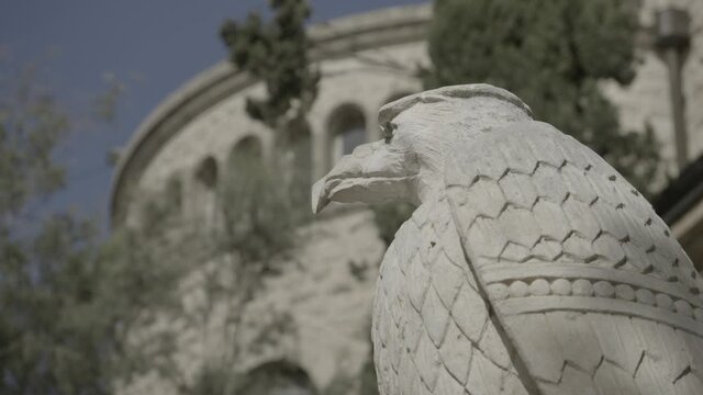 A close up on an eagle stone statue with an impressive old stone building in the background, where the trees and their shadows are moving, a 4K clip, October 6, 2020, East Jerusalem, Israel.