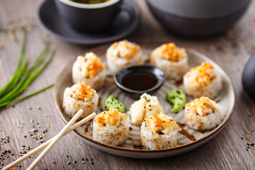Baked sushi maki rolls with prawns and crab on a plate with chopsticks, soy sauce, wasabi and ginger. Japanese traditional fish food closeup served for lunch in modern gourmet restaurant