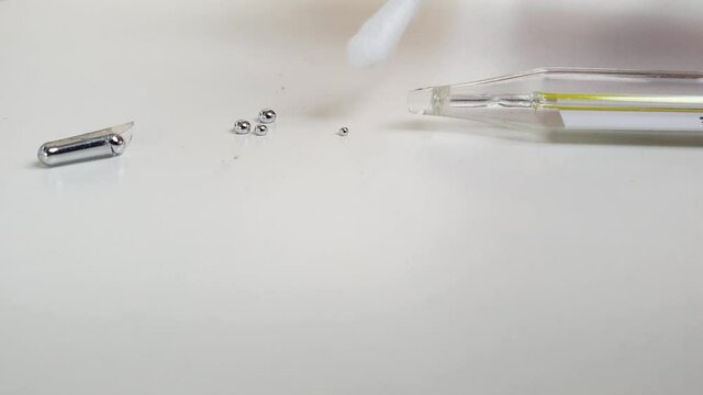 Mercury thermometer broken, close-up on white background. Remove mercury from  table  surface, combining small metal balls