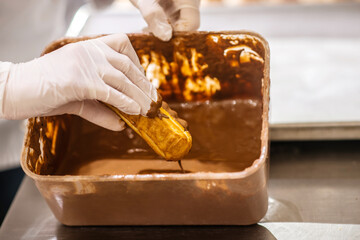 Hands dipping eclair in chocolate fondant in tray