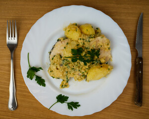 Delicious Hake served on a green sauce with parsley leaves in a white dish with cutlery. Top View
