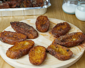 Traditional homemade and Delicious Spanish Torrijas making a circle on a round wooden plate decorated with its ingredients and a tray of torrijas
