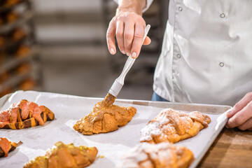 Male hand with brush touching croissant surface
