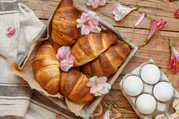 Fresh croissants and flowers in a tray on a wooden table