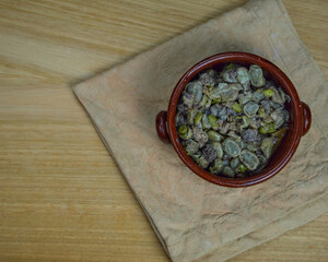 Habas a la Catalana, Tasty stew of beans in a clay bowl on a wooden table and a brown napkin. Top view