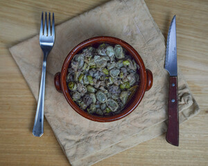 Habas a la Catalana, Tasty stew of beans in a clay bowl and cutlery on a wooden table and a brown napkin. Top view