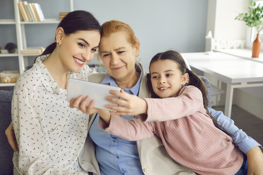 Happy family moments. Little girl taking a selfie with her mother and grandmother. Child with a phone in his hands makes a family portrait depicting three generations. Family and relations concept.