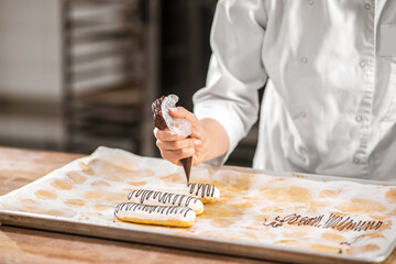 Confectioners hand squeezing pastry bag over eclair