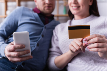 Cropped view of cellphone and credit card in hands of couple on blurred background
