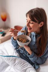 Woman eating cereal while having breakfast in bed