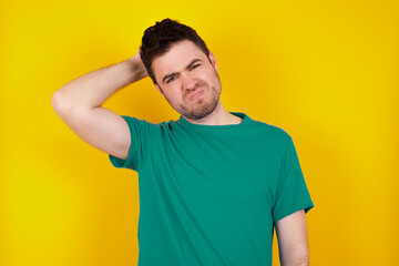 young Caucasian man wearing green T-shirt against yellow wall being confused and wonders about something. Holding hand on her head, uncertain with doubt. Pensive concept.