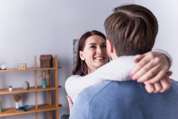 Adult woman smiling while hugging husband on blurred foreground at home