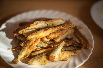 fried capelin on a white plate, small fish in corn breading on a white plate, simple homemade food concept, home cooking fish cooking