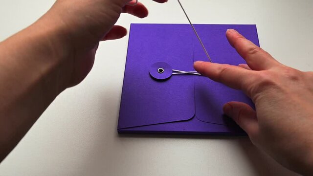 Person unties thin lace on blue paper envelope or folder. 