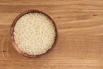 sesame seeds in bowl on wooden background, top view