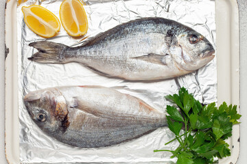 Raw dorado fish with lemon and parsley in a dish on the table. Top View