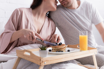 Cropped view of woman holding cutlery near pancakes and husband on blurred background on bed