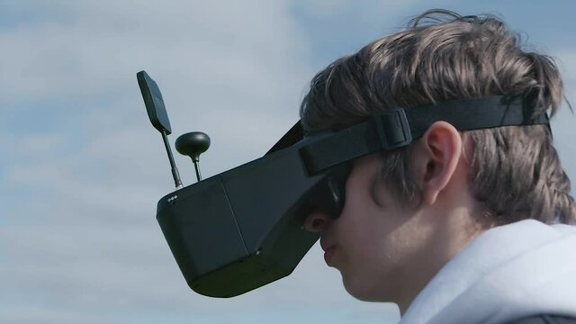 Teenage boy flying FPV acrobatic drone. Close up of a young man controlling a drone with goggles. Piloting a racing drone. VR spectacles with antennas. View at close range of teenager with goggles.