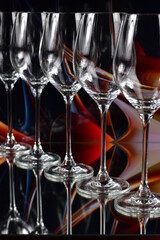 Diagonal of five empty wine glasses on a colored abstract background and reflective surface