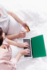 Top view of couple using laptop with green screen and credit card on bed