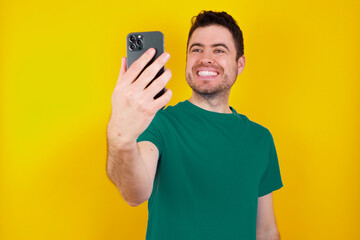 young handsome caucasian man wearing green t-shirt against yellow background smiling and taking a...