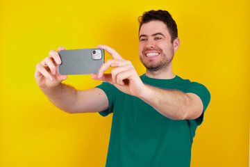 young handsome caucasian man wearing green t-shirt against yellow background taking a selfie to...