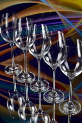 Diagonal of five empty wine glasses on a colored abstract background and reflective surface