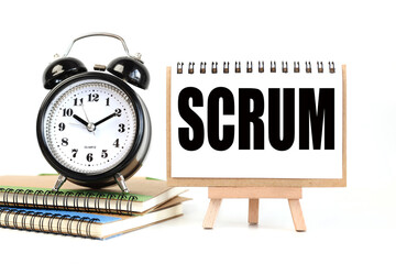 Scrum. Text on white notepad paper on a stand next to our desk clock on a sideboard. on white background