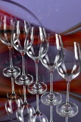 Diagonal of five empty wine glasses on a colored abstract background and reflective surface