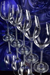 Diagonal of five empty wine glasses on a colored abstract background and reflective surface
