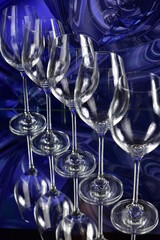 Diagonal of five empty wine glasses on a colored abstract background and reflective surface