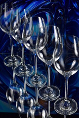 Diagonal of five empty wine glasses on a colored abstract background and reflective surface