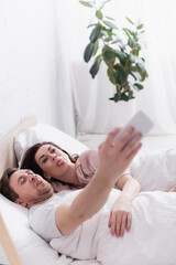 Obraz na płótnie Canvas Adult couple sticking out tongues while taking selfie in bed