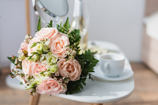 Selective focus of wedding bouquet near coffee cup and mirror on blurred background.