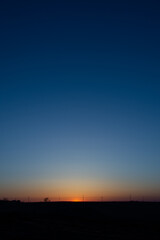 Fototapeta premium A setting sun dips below the horizon in an almost cloudless blue sky.