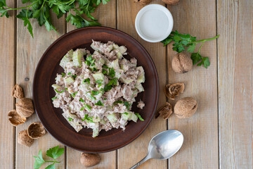 A hearty lunch: salad of canned fish and celery in a clay bowl on a wooden table