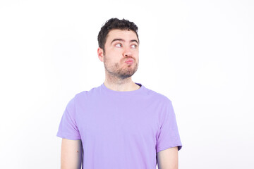 Obraz premium young handsome caucasian man wearing purple t-shirt against white background, looks pensively aside, plans actions after university, imagines what to do Thinks over about new project.
