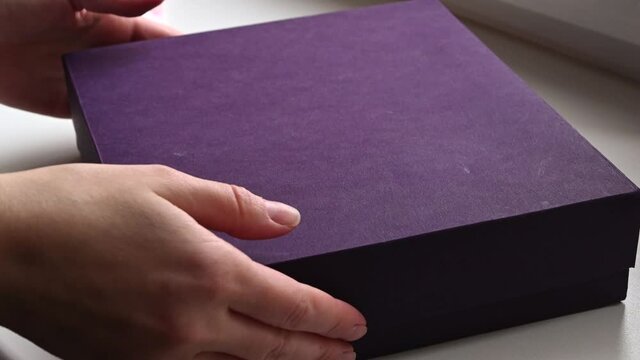 Person unpacking gift box with blue envelope inside tied on string closure. 