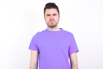 Fototapeta premium young handsome caucasian man wearing purple t-shirt against white background frowning his eyebrows being displeased with something.