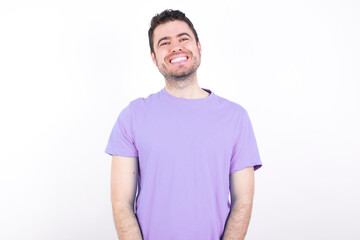 Obraz premium young handsome caucasian man wearing purple t-shirt against white background with broad smile, shows white teeth, feeling confident rejoices having day off.