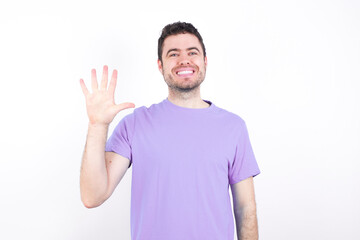 young handsome caucasian man wearing purple t-shirt against white background showing and pointing up with fingers number five while smiling confident and happy.