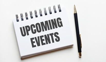 On a light background, a white notebook with are words UPCOMING EVENTS and a pen.