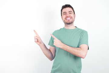 young handsome caucasian man wearing green t-shirt against white background with positive expression, indicates with fore finger at blank copy space for your promotional text or advertisement.