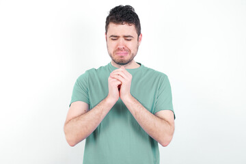 Sad young handsome caucasian man wearing green t-shirt against white background feeling upset while spending time at home alone staring at camera with unhappy or regretful look.