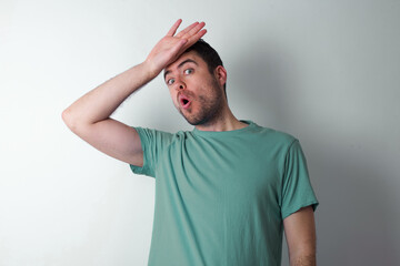 young handsome caucasian man wearing green t-shirt against white wall wiping forehead with hand making phew gesture, expressing relief feels happy that he prevented huge disaster. It was close enough